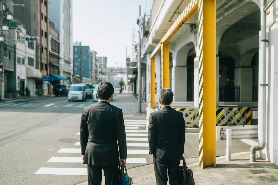 スーツを着た2人のビジネスマンが日本の都会の風景の中で道路を横断しており、日常の都市生活を反映しています。