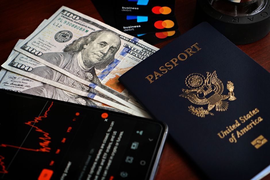 100 ドル札、クレジットカード、株価データを表示しているスマートフォンが入った米国のパスポート。