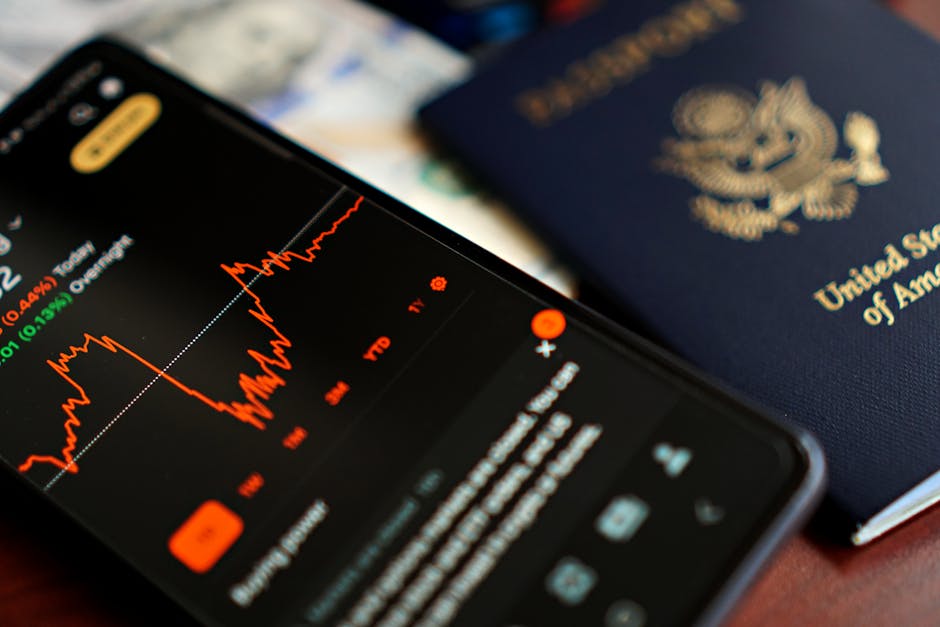 旅行と金融のテーマを示唆する、米国のパスポートの横に株価データを表示したスマートフォンのクローズアップ。