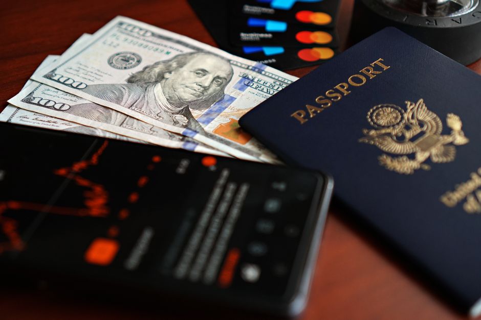 パスポート、米ドル、クレジットカードなどの旅行の必需品をテーブルの上に平らに並べた画像。