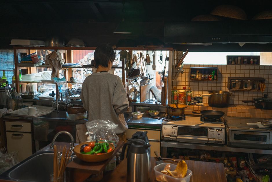 日本の伝統的な台所で、さまざまな道具や食材を使って料理をする人。