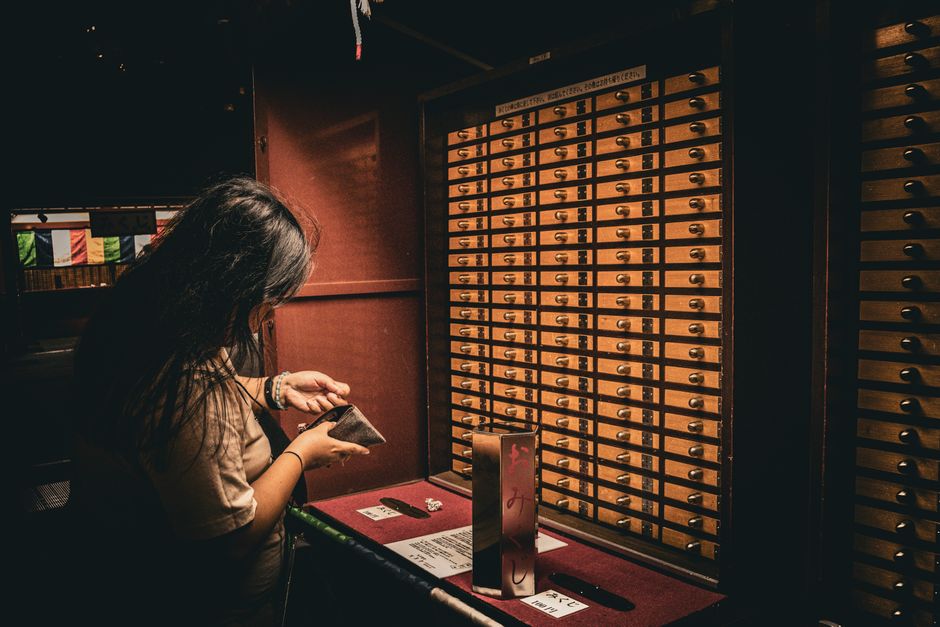引き出しやお札が置かれた伝統的で雰囲気のある空間で、女性がおみくじをチェックしています。
