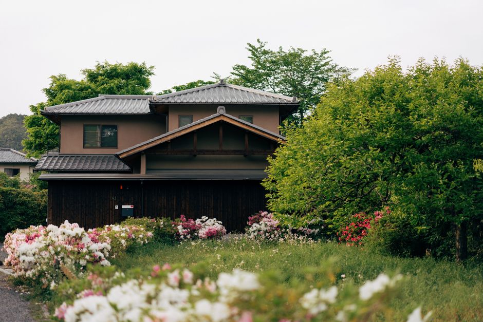 豊かな緑と咲き誇る花々に囲まれた、穏やかな日本の伝統的な家屋のイメージ。