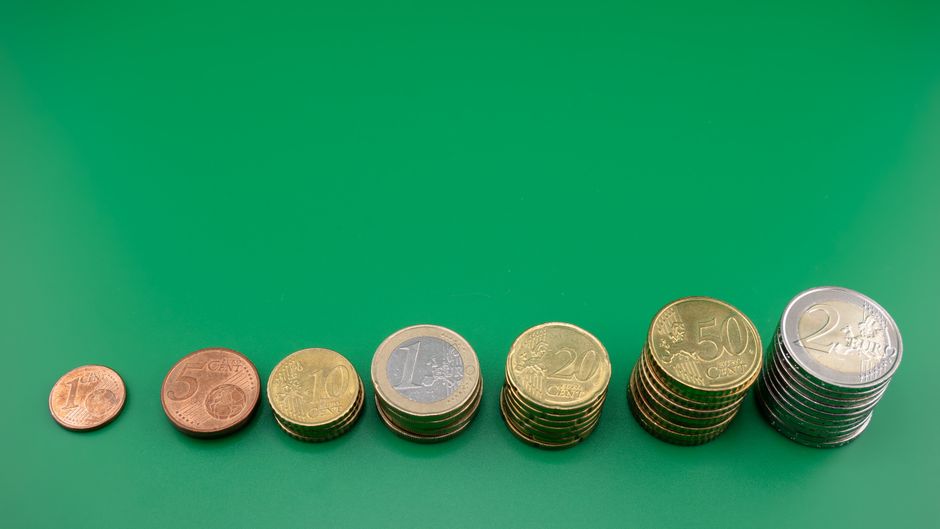 鮮やかな緑色の背景に、様々なユーロ硬貨が少しずつ積み重ねられている。