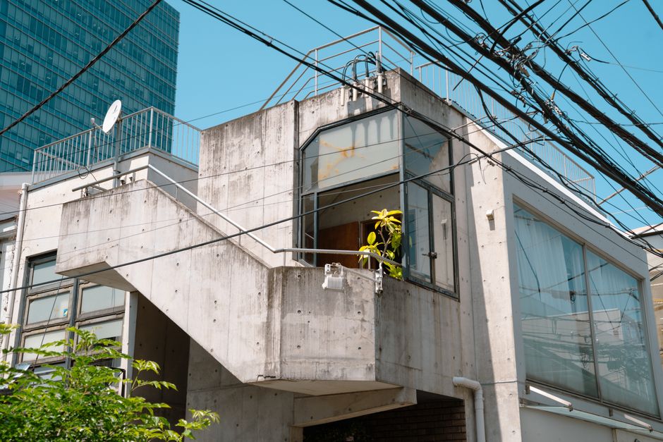 東京にある、屋上デッキを備えたモダンなコンクリート造りの住宅。澄み渡る青空の下、都会的なスタイルとミニマリストなスタイルが見事に融合している。