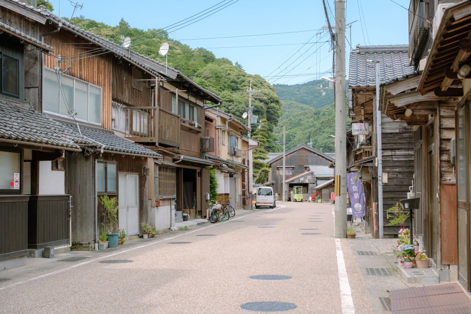 木造家屋と緑豊かな木々が立ち並ぶ、穏やかな日本の伝統的な街並み。